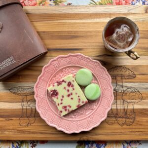 Teak cutting board with a plate of sweet treats and a cup of tea.